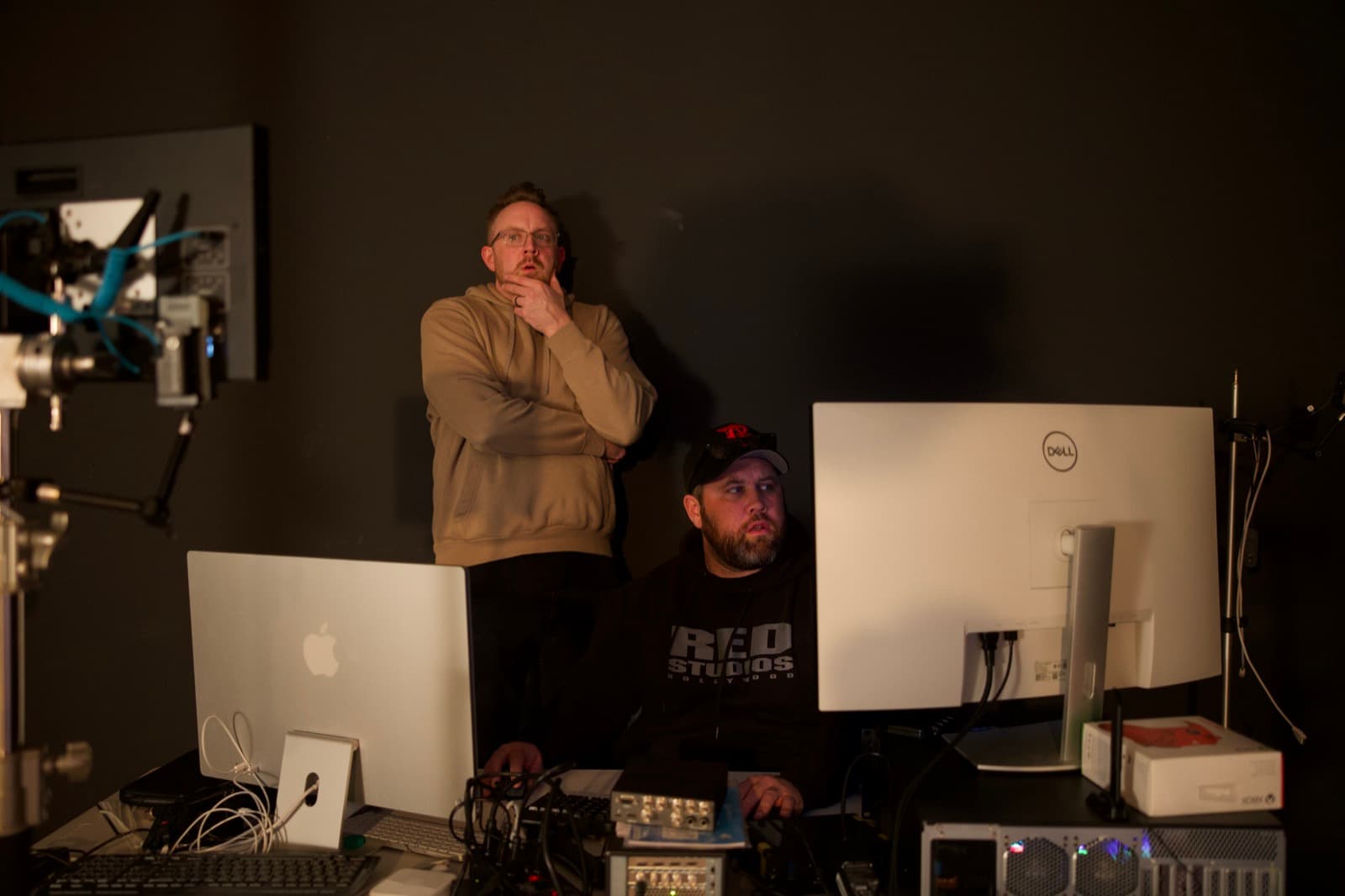 Two crew members confer at a control workstation with a laptop and dual monitors in a dimly lit studio