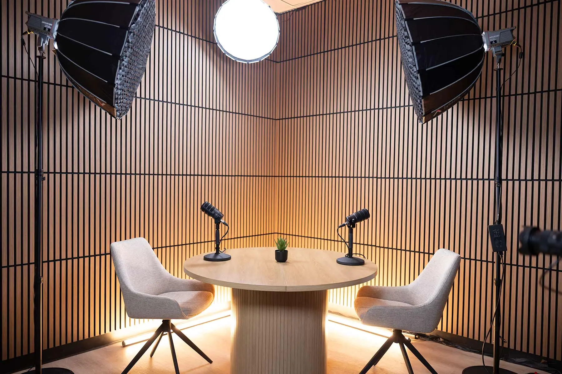 The Content Studio at Big Screen Studios: a wood-slatted podcast set with two soft chairs, table microphones, and softbox lighting.