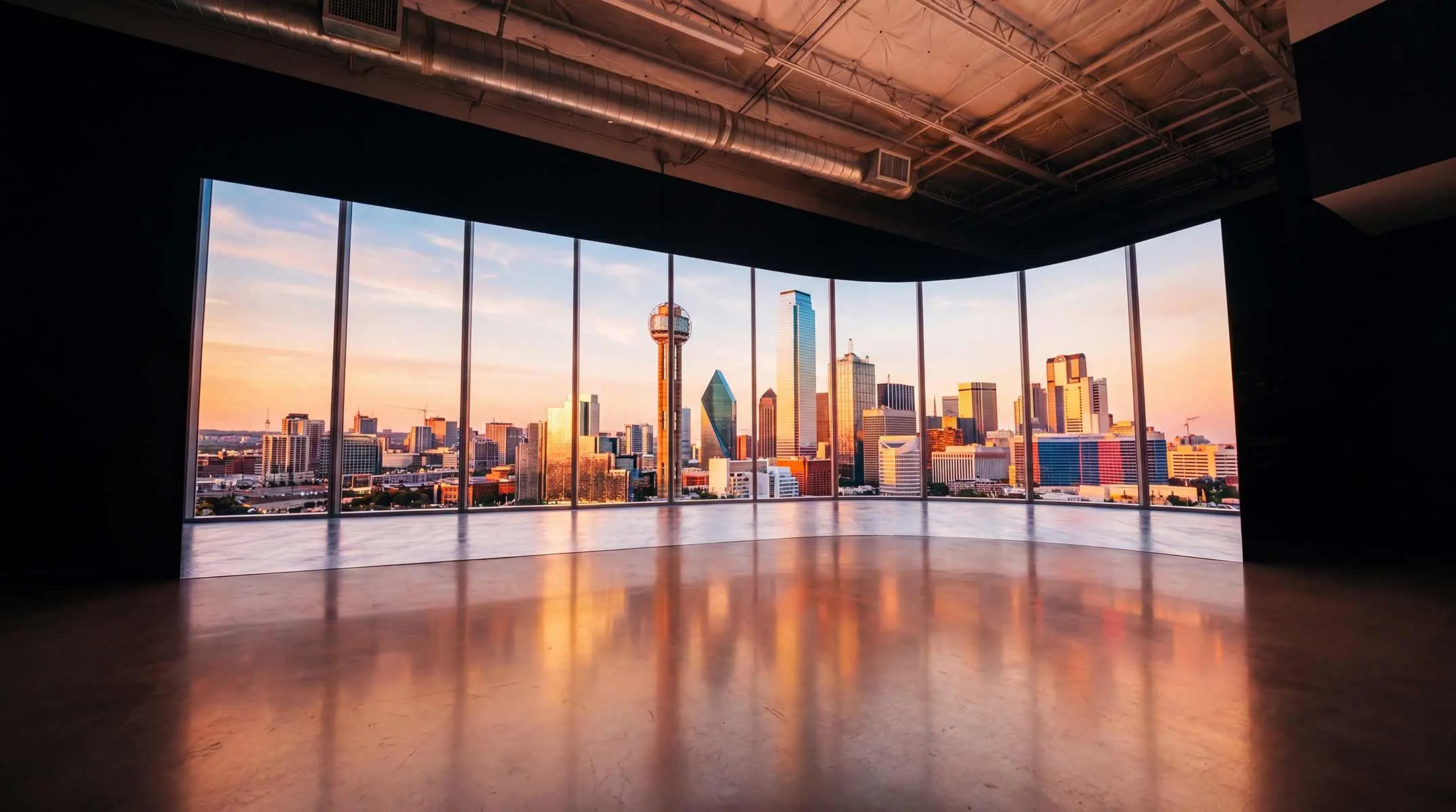 The Big Screen Stage: a curved LED volume wall displaying the Dallas skyline at sunset above a polished, empty stage floor.