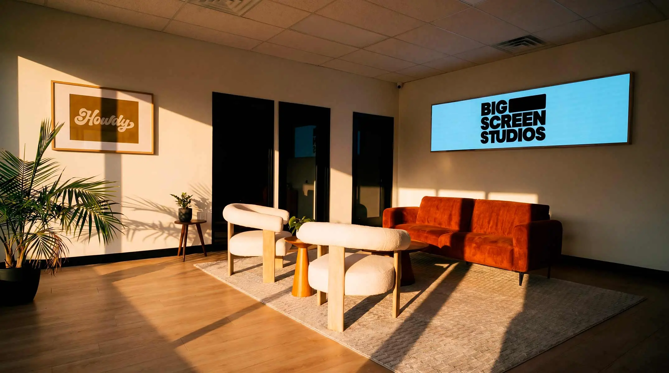 The lobby at Big Screen Studios: sunlit lounge seating with a rust sofa and a lit Big Screen Studios sign on the wall.