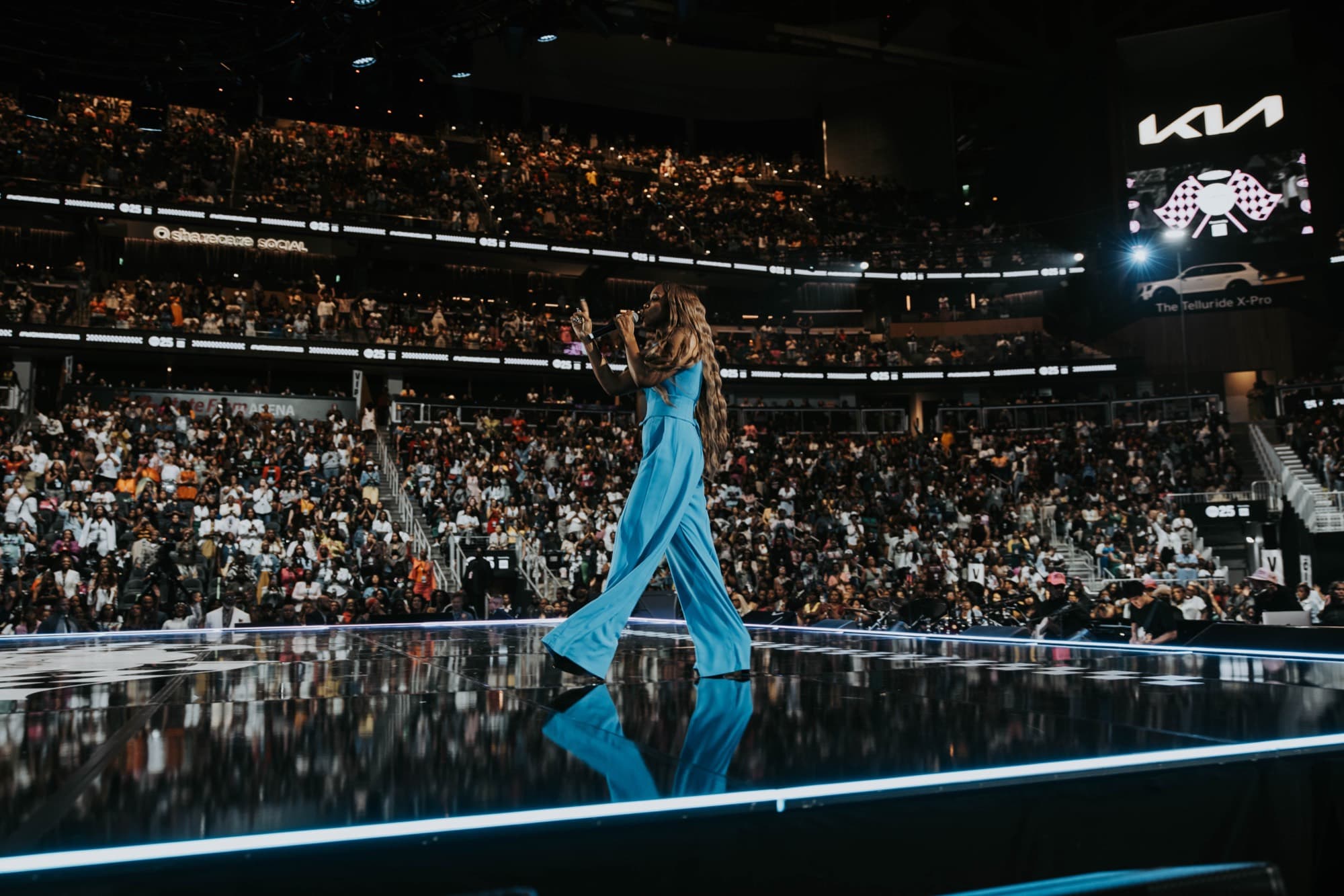 A performer crossing the glossy Woman Evolve stage with the packed arena bowl behind