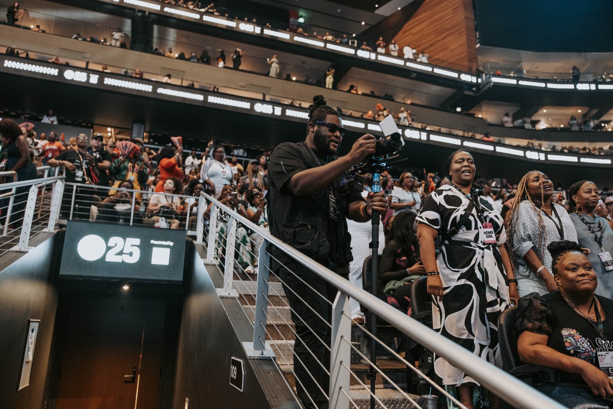 A Griffith Media operator shooting from the arena stairs with the crowd stretching below