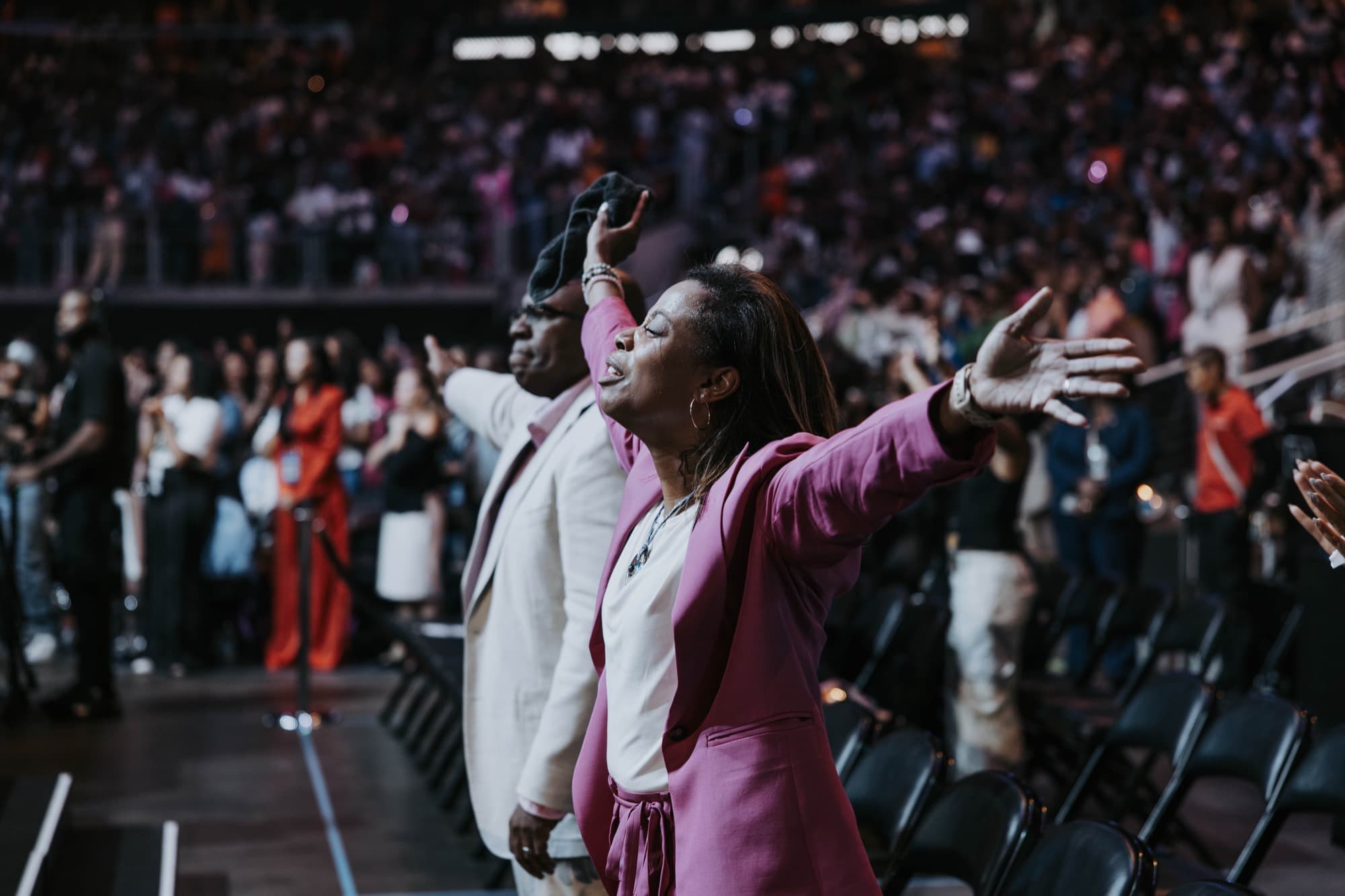 A worship service filling a darkened arena, hands raised toward the stage