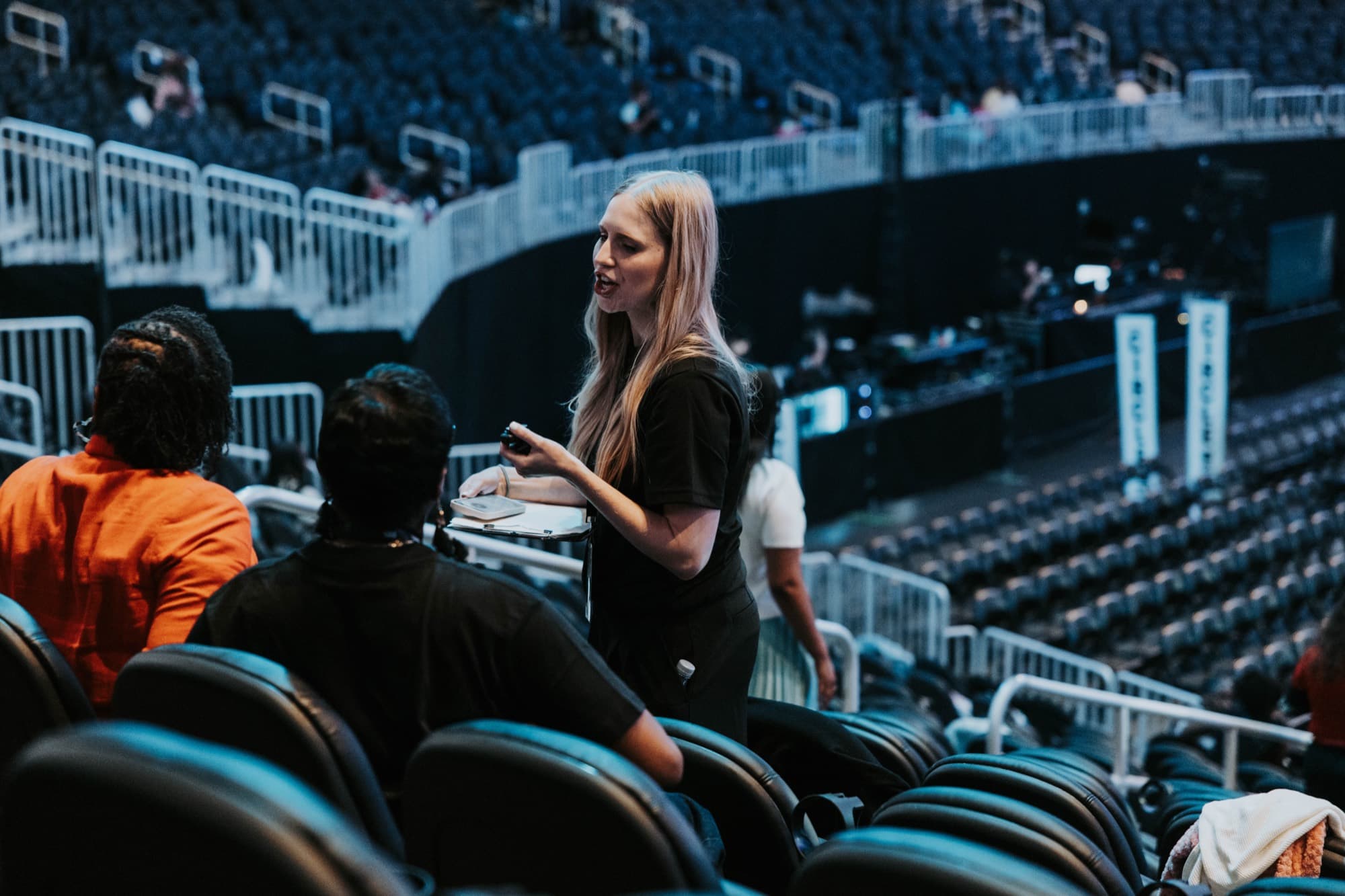 Grace Griffith with a clipboard talking with seated attendees in the arena