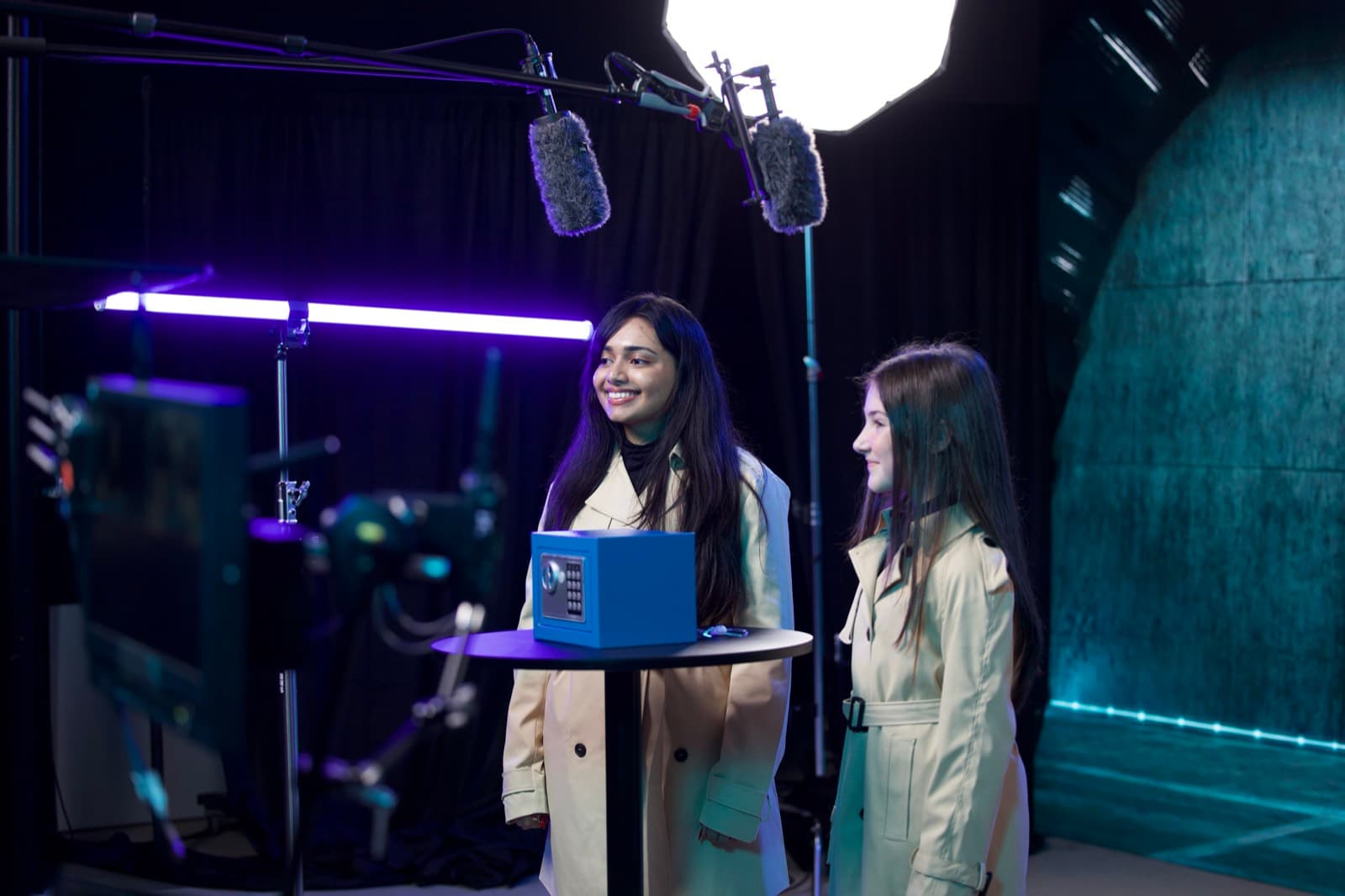Two actors on set beside the prize safe, boom mics overhead and the LED wall lighting the scene